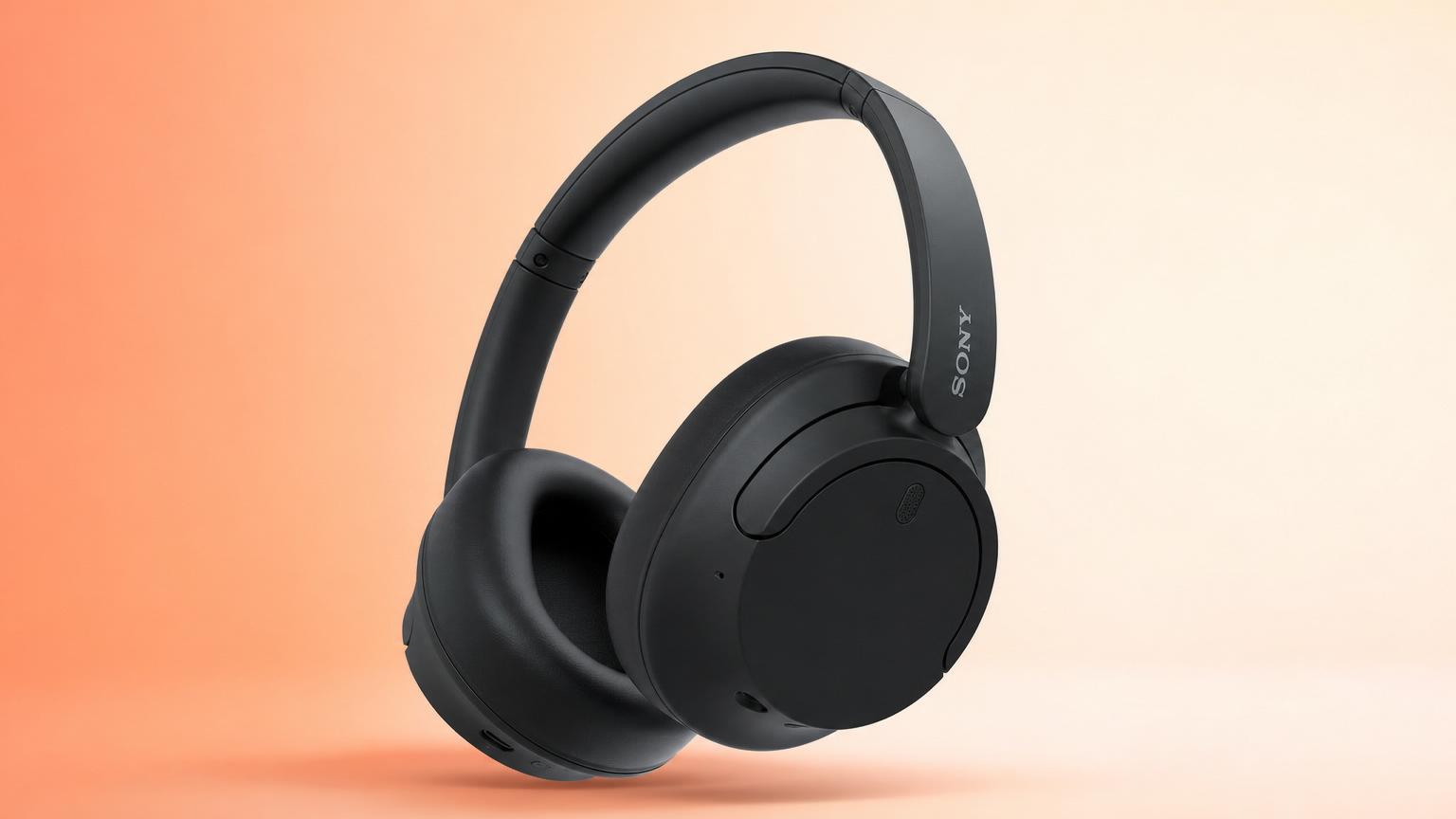 Fone over-ear preto com cancelamento de ruído sobre mesa clara ao lado de um notebook